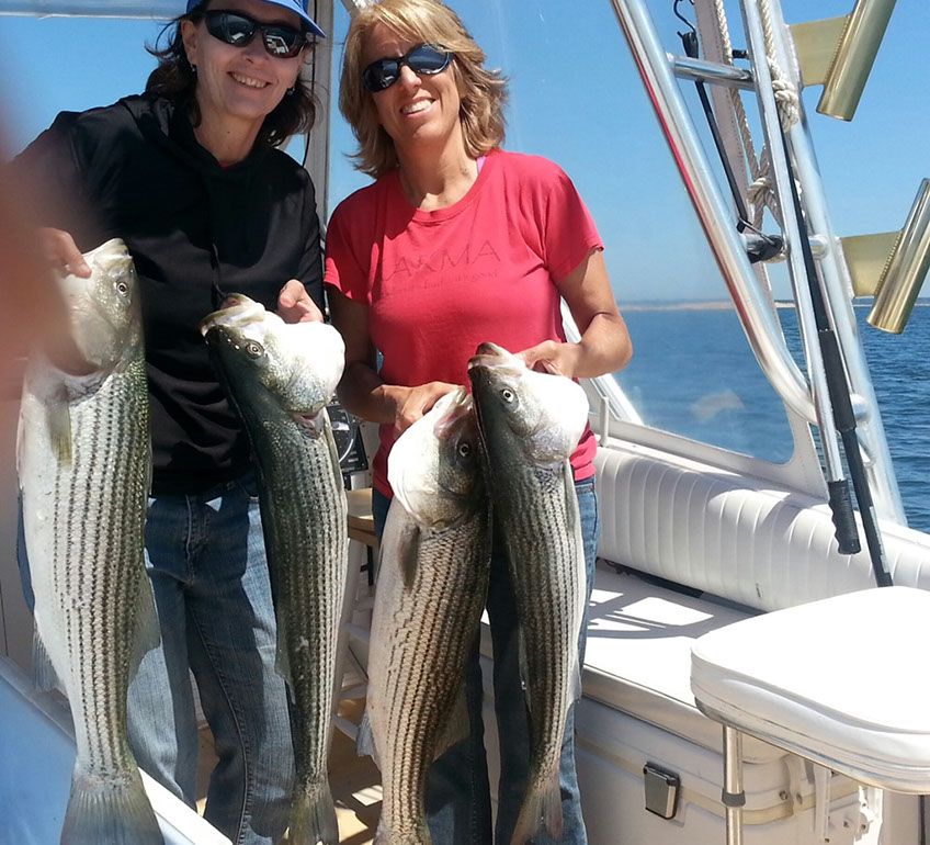 Two Women Holding Striper Fishes